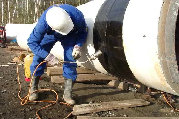 Technician heating a field joint on a large-diameter pipe