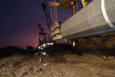 Coated pipe lifted on rollers at an HDD site at dusk