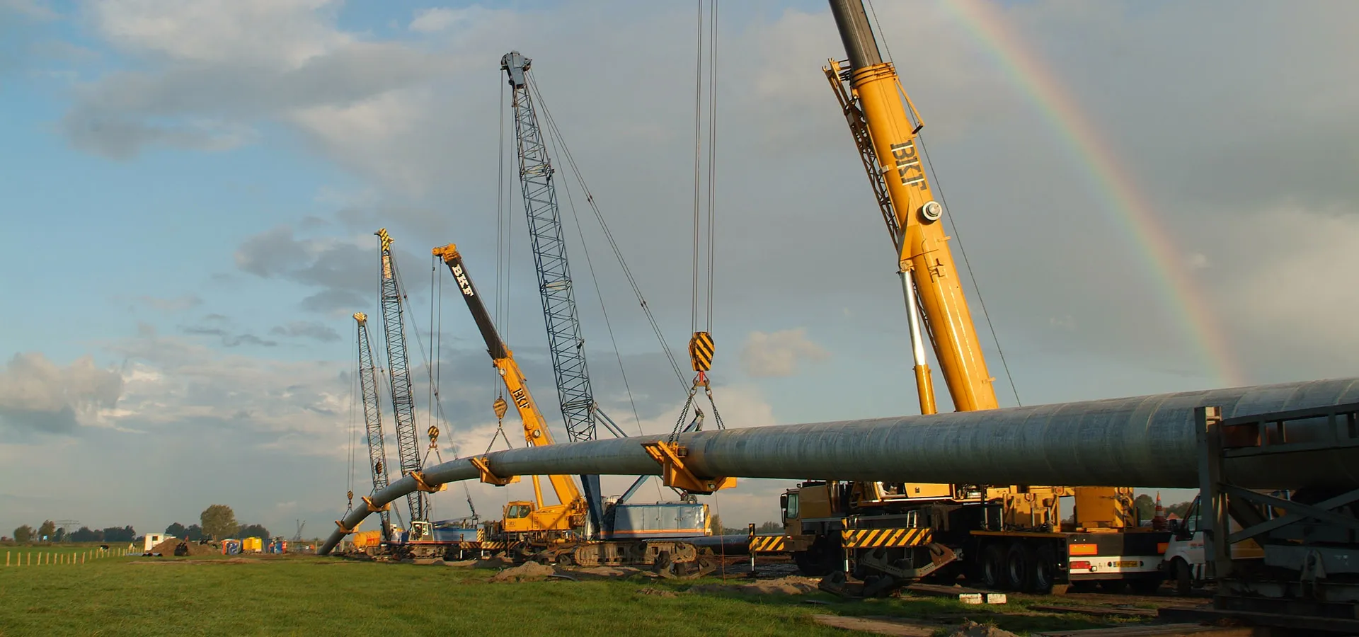 A coated pipe string lifted by cranes for a horizontal directional drilling, with a rainbow behind it